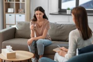a woman sits on a couch and looks down while talking to her therapist about her struggles in her ptsd treatment